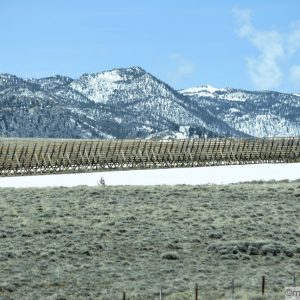 Over 10 feet tall snow fence in front miles in front of a mountain range
